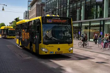Un autobus di trasporto pubblico di colore giallo brillante su una strada cittadina trafficata, con ciclisti e pedoni.
