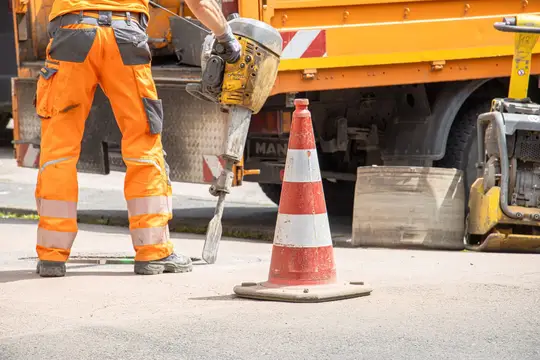 Operaio edile con martello pneumatico accanto a un cono stradale su una strada cittadina